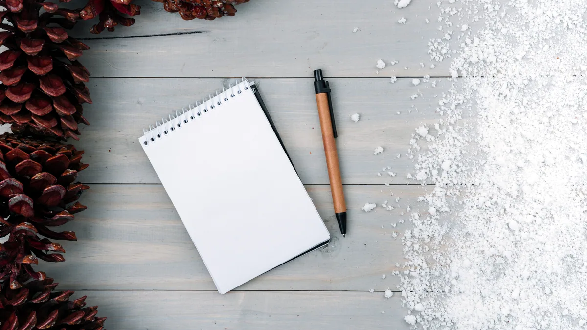 A clipboard and a marker lying on a flat sheet of snow, a small group visible in the distance.