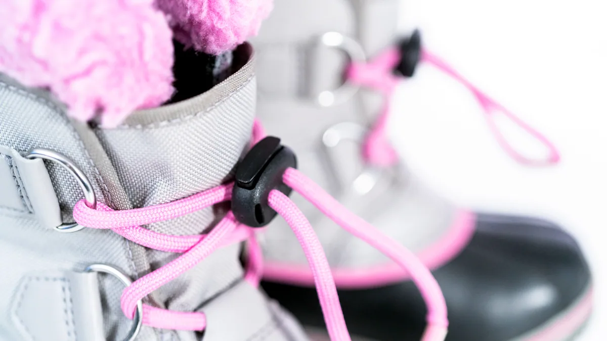 A pair of stiff snowboard boots with laces cinched tight, sitting on a stone step.