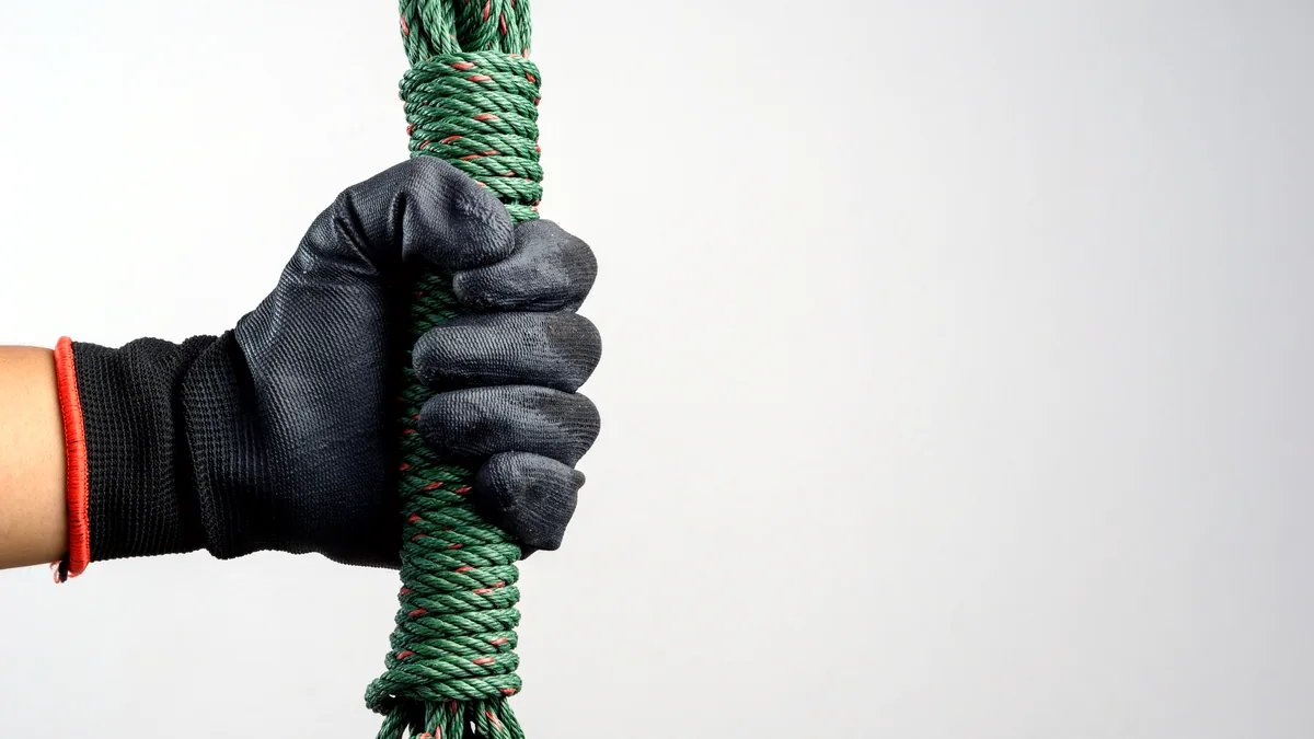 A pair of insulated gloves gripping a rough rope, snowflakes catching the light around them.