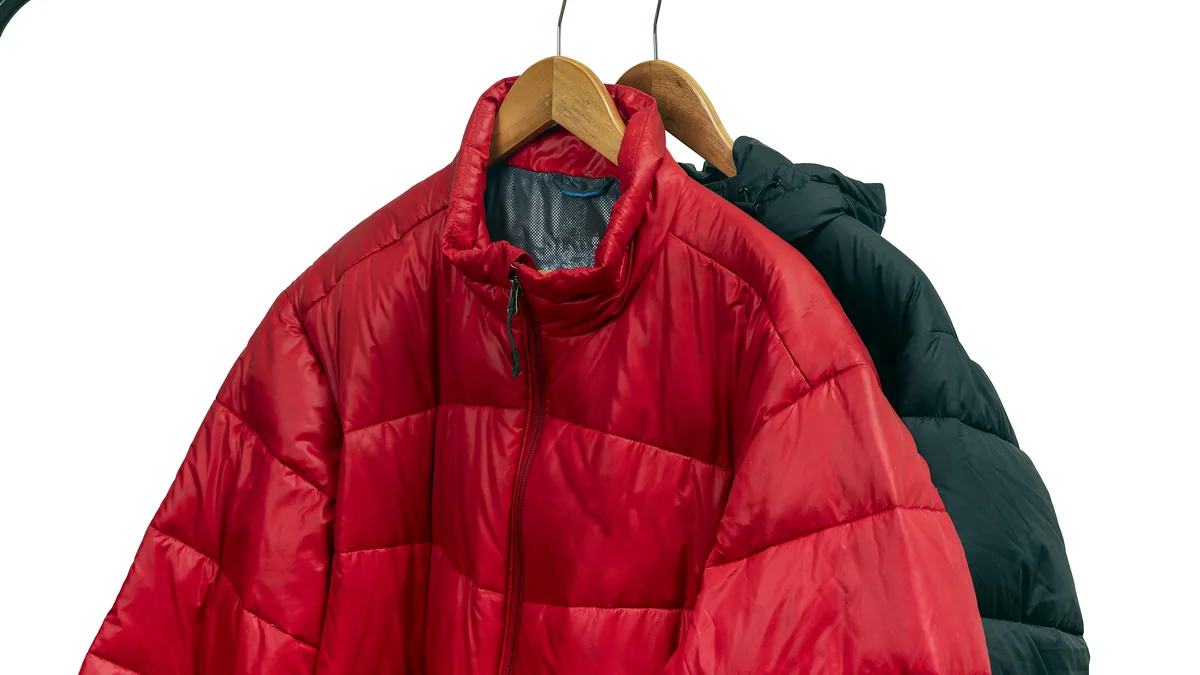 A bright red insulated jacket hanging on a metal hook against a concrete wall.