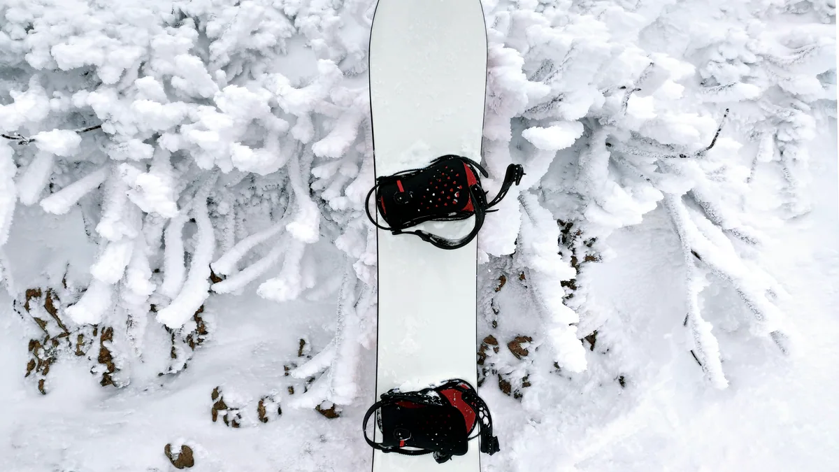 A snowboard standing upright in soft powder, a small boot print trail leading up to it.