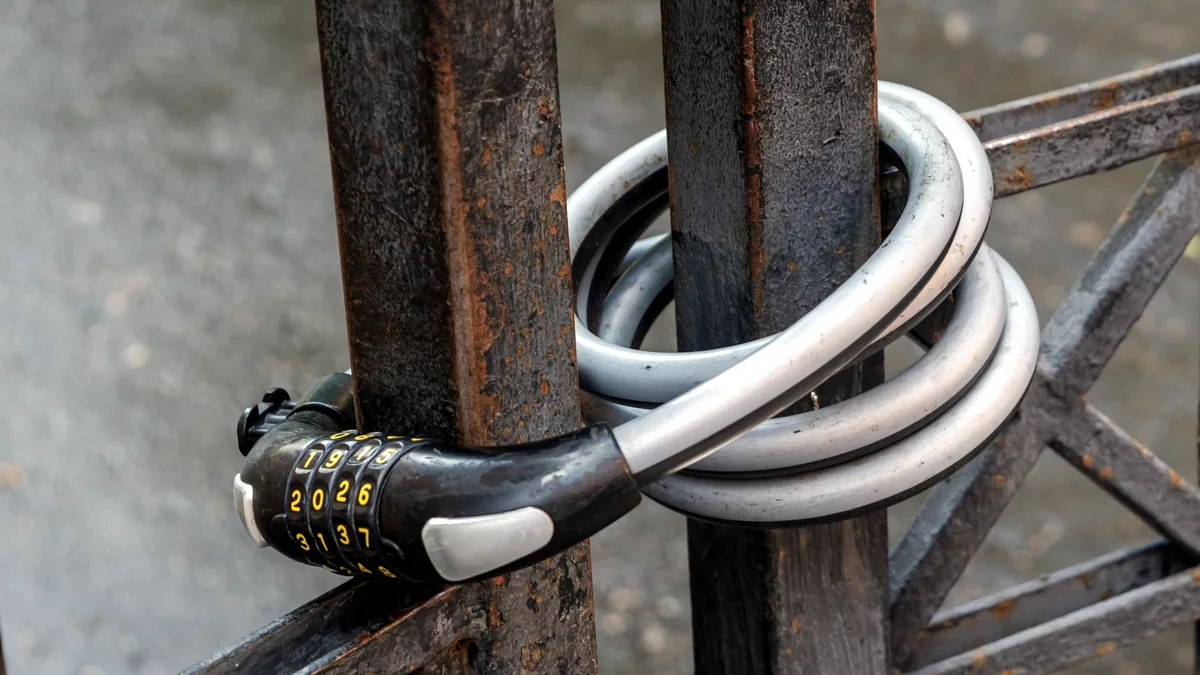 A heavy cable lock wrapped around a metal fence post, snow dusting the ground below.
