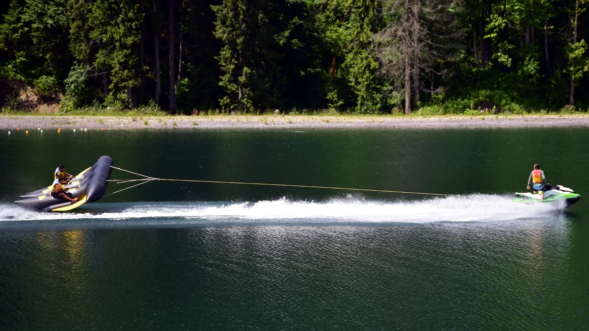A single waterski slicing through a calm lake, throwing up a fan of white spray.